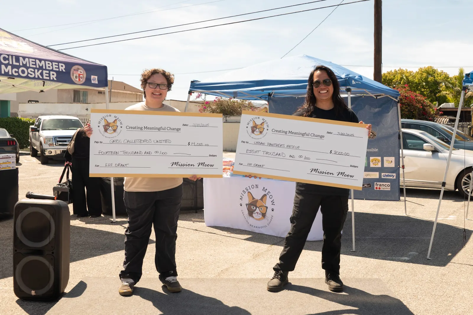 Two rescue leaders smile holding giant Mission Meow checks for $14,000 and $8,000